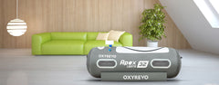 OXYREVO Apex 32 portable hyperbaric chamber in a modern living room setting with a green sofa and plant.