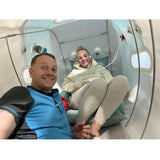 Two people sitting inside of  seated portable hyperbaric chamber.  Inside forward 90